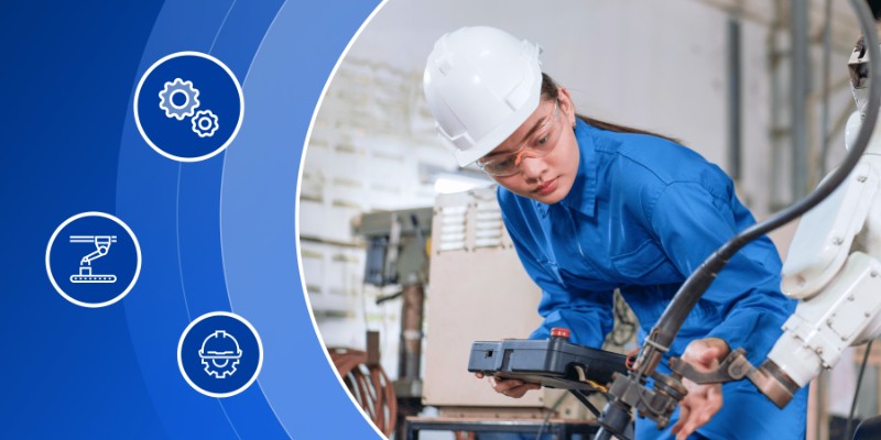 Female engineering student in a blue jumpsuit and hard hat working with robotic equipment in a high-tech lab.