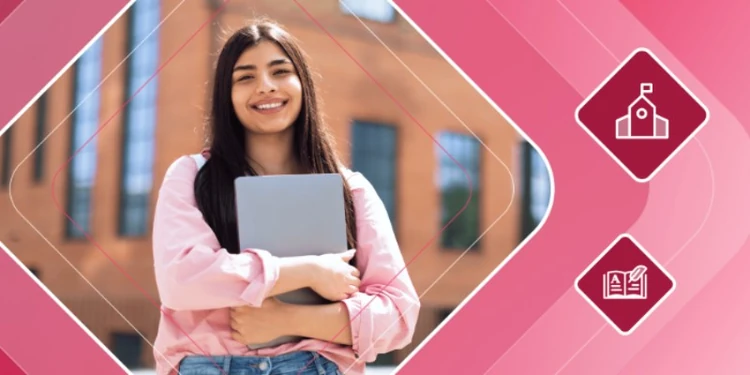 Smiling student holding a laptop on a university campus.