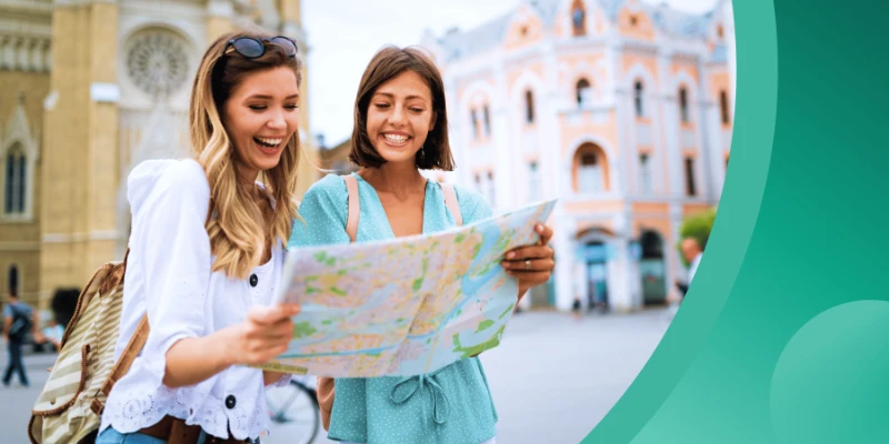 Two smiling young women looking at a open paper map together in a European city square with historical buildings in the background, set alongside a green graphic overlay.